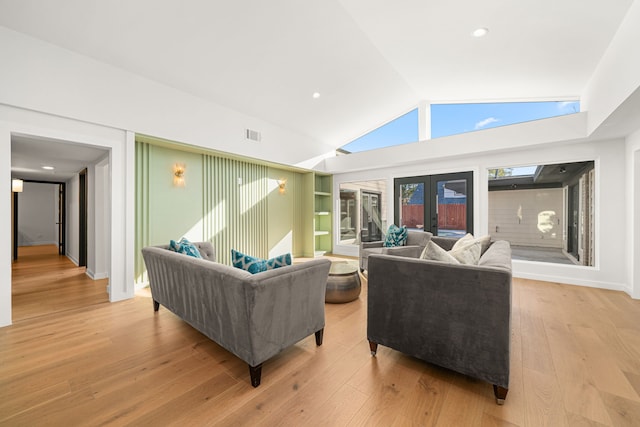 living room featuring vaulted ceiling, built in features, light hardwood / wood-style flooring, and french doors