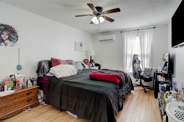 bedroom with a wall mounted AC, a textured ceiling, light hardwood / wood-style floors, and ceiling fan