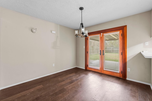 unfurnished dining area with dark hardwood / wood-style floors, a textured ceiling, and an inviting chandelier