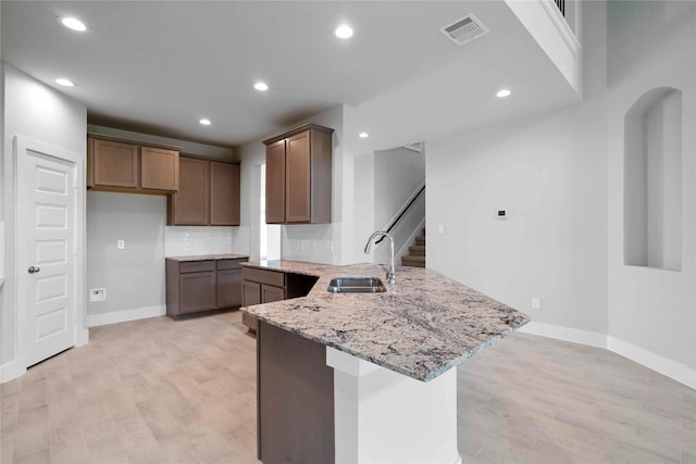 kitchen featuring sink, light stone counters, backsplash, kitchen peninsula, and light hardwood / wood-style floors