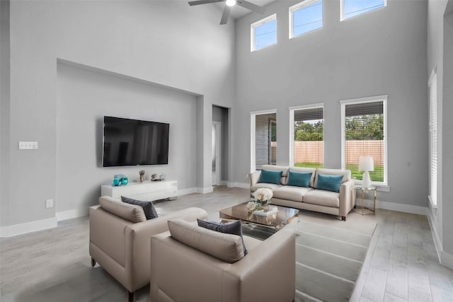 living room featuring ceiling fan, light wood-type flooring, and a towering ceiling