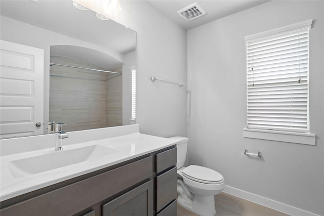 bathroom with toilet, vanity, plenty of natural light, and tiled shower