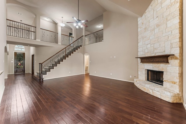 unfurnished living room with hardwood / wood-style flooring, ceiling fan, a stone fireplace, and high vaulted ceiling