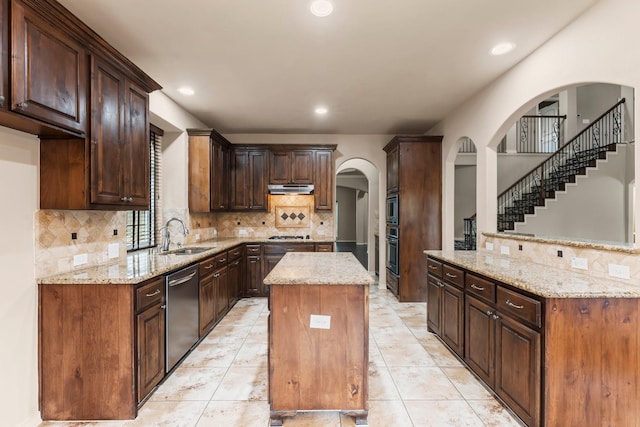 kitchen with dark brown cabinetry, sink, light stone counters, a center island, and appliances with stainless steel finishes