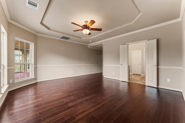 empty room with dark wood-type flooring, ceiling fan, crown molding, and a raised ceiling