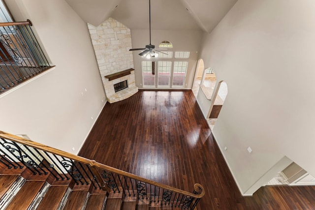 unfurnished living room featuring wood-type flooring, a stone fireplace, ceiling fan, and high vaulted ceiling