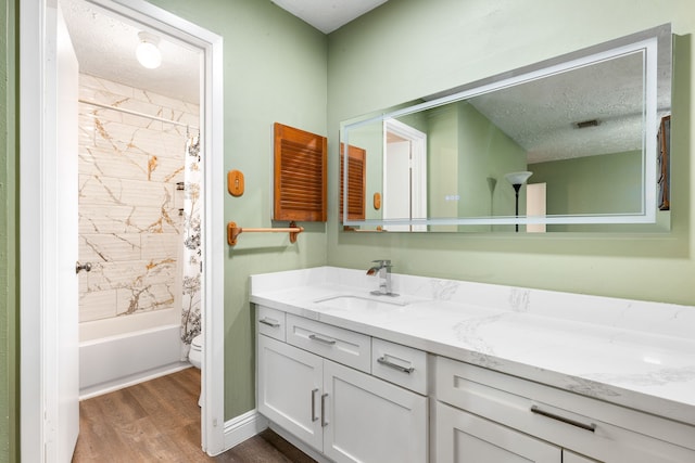 full bathroom with shower / tub combo with curtain, hardwood / wood-style flooring, vanity, toilet, and a textured ceiling