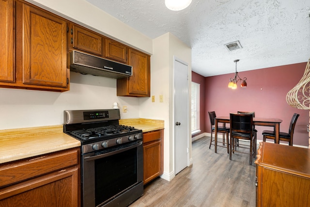 kitchen featuring hardwood / wood-style flooring, stainless steel gas range, hanging light fixtures, and a textured ceiling