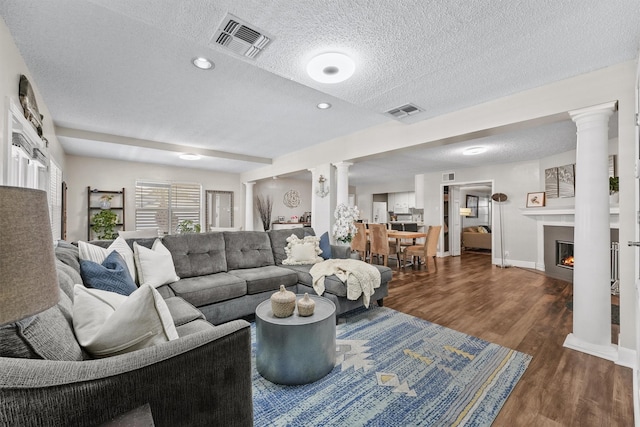 living room with a textured ceiling, dark hardwood / wood-style flooring, and ornate columns