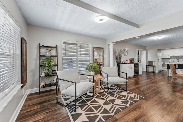 living area featuring dark wood-type flooring, a textured ceiling, beverage cooler, and decorative columns