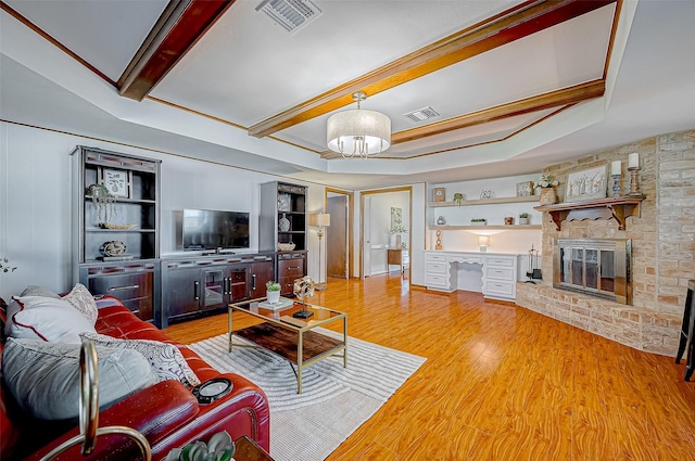 living room featuring light hardwood / wood-style floors, a raised ceiling, built in features, and a fireplace