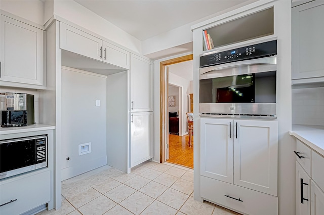 kitchen featuring oven, white cabinetry, built in microwave, and light tile patterned floors