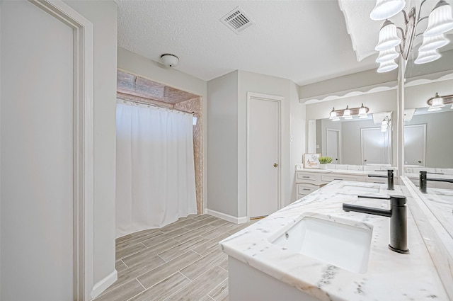 bathroom featuring a notable chandelier, vanity, and a textured ceiling