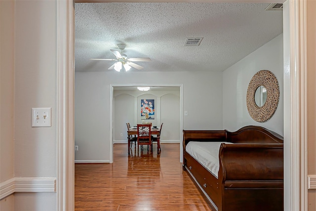 bedroom with ceiling fan, wood-type flooring, and a textured ceiling