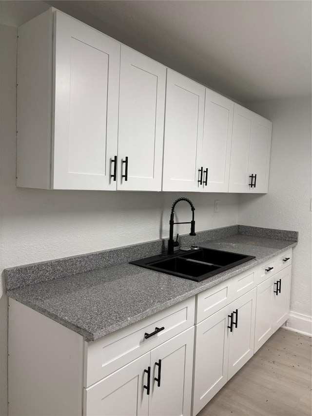 kitchen with light hardwood / wood-style floors, white cabinetry, and sink