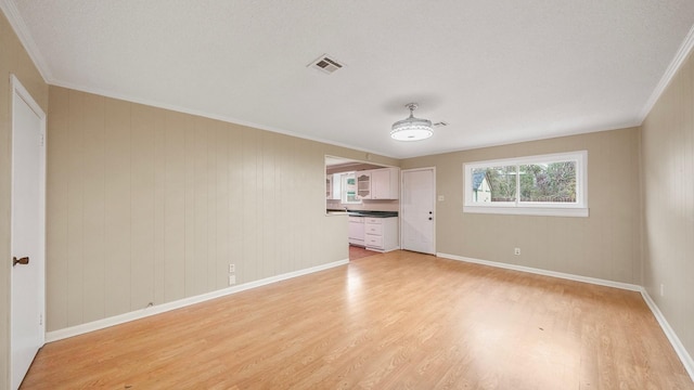 empty room featuring a textured ceiling, light hardwood / wood-style floors, and crown molding