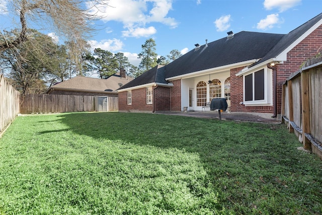 rear view of house with a fenced backyard, brick siding, a yard, a chimney, and a patio area