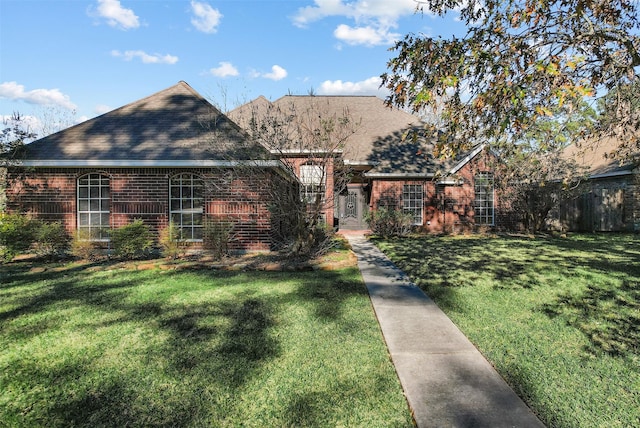 view of front of property featuring brick siding, roof with shingles, and a front yard