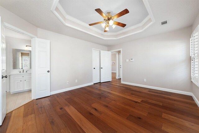 unfurnished bedroom featuring a tray ceiling, ceiling fan, sink, hardwood / wood-style flooring, and connected bathroom