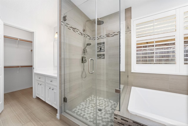 bathroom with a stall shower, a walk in closet, a bath, and vanity