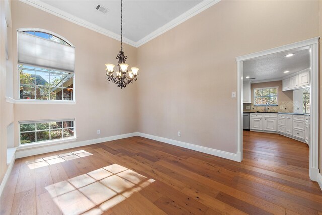 unfurnished dining area with a notable chandelier, sink, wood-type flooring, and crown molding