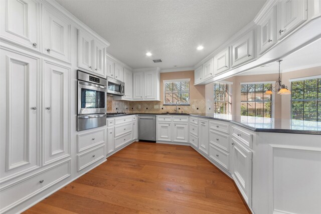 kitchen featuring white cabinets, light wood-type flooring, appliances with stainless steel finishes, tasteful backsplash, and kitchen peninsula