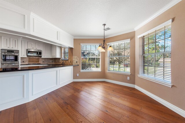 kitchen with an inviting chandelier, white cabinets, light hardwood / wood-style flooring, appliances with stainless steel finishes, and decorative light fixtures