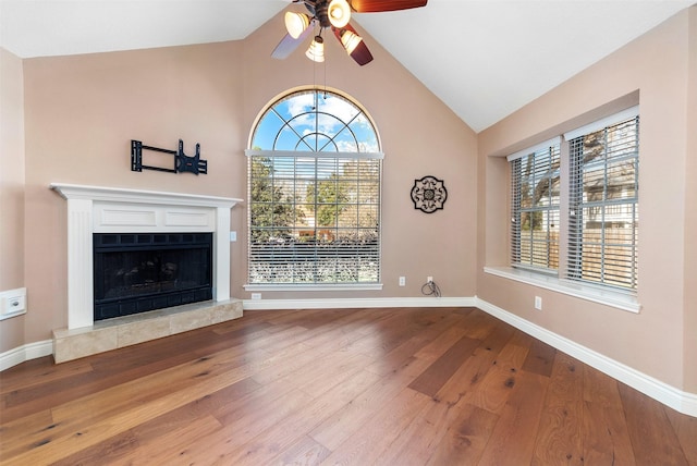 unfurnished living room featuring lofted ceiling, hardwood / wood-style floors, a tiled fireplace, and baseboards