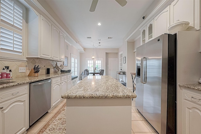 kitchen with decorative backsplash, light tile patterned floors, a kitchen island, white cabinetry, and stainless steel appliances