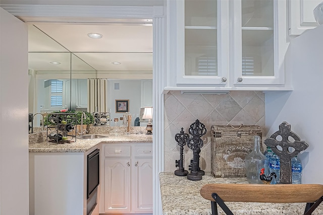 bar with backsplash, light stone countertops, white cabinetry, and sink