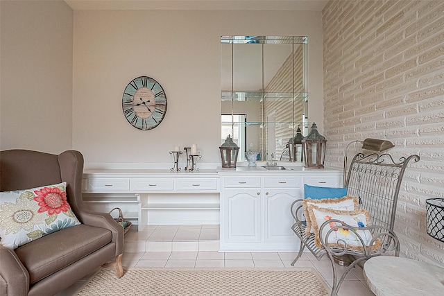 living area featuring light tile patterned floors, sink, and brick wall