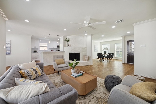 living room with ceiling fan, light hardwood / wood-style floors, ornamental molding, and a fireplace