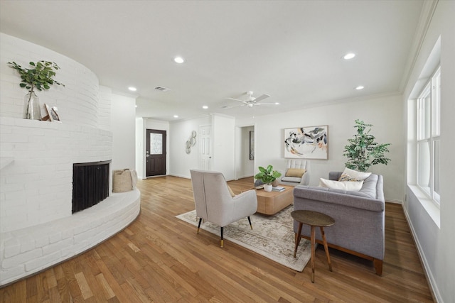 living room with hardwood / wood-style flooring, ceiling fan, crown molding, and a brick fireplace