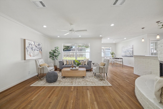 living room with light hardwood / wood-style floors, a brick fireplace, ceiling fan, and ornamental molding