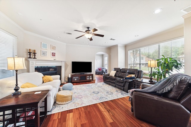 living room featuring wood-type flooring, ceiling fan, ornamental molding, and a tiled fireplace