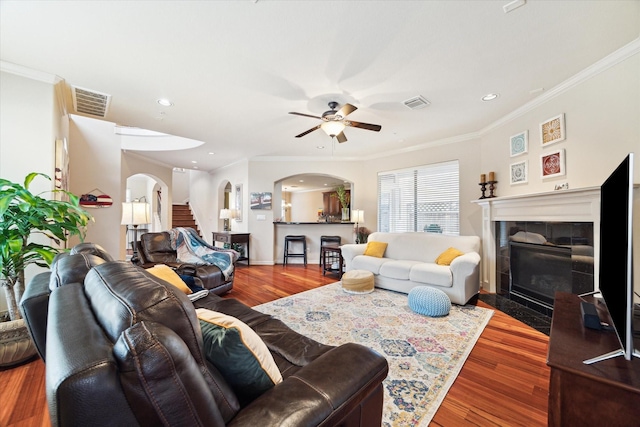 living room with hardwood / wood-style floors, ceiling fan, crown molding, and a tiled fireplace