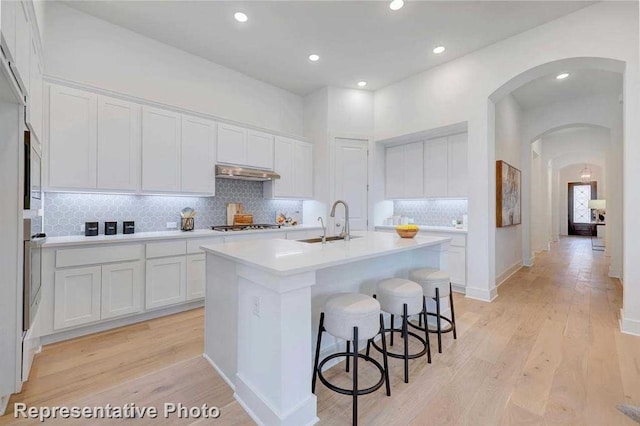 kitchen featuring sink, a center island with sink, white cabinetry, and range hood