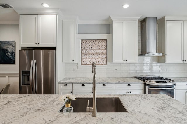 kitchen featuring white cabinetry, decorative backsplash, light stone countertops, wall chimney range hood, and appliances with stainless steel finishes