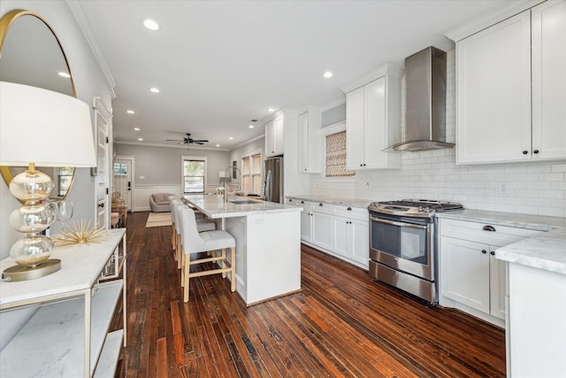 kitchen with stainless steel appliances, white cabinets, wall chimney exhaust hood, ceiling fan, and light stone countertops