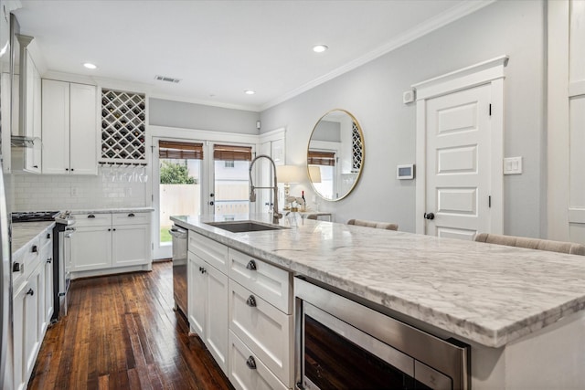 kitchen with a kitchen island with sink, stainless steel appliances, light stone countertops, sink, and white cabinetry