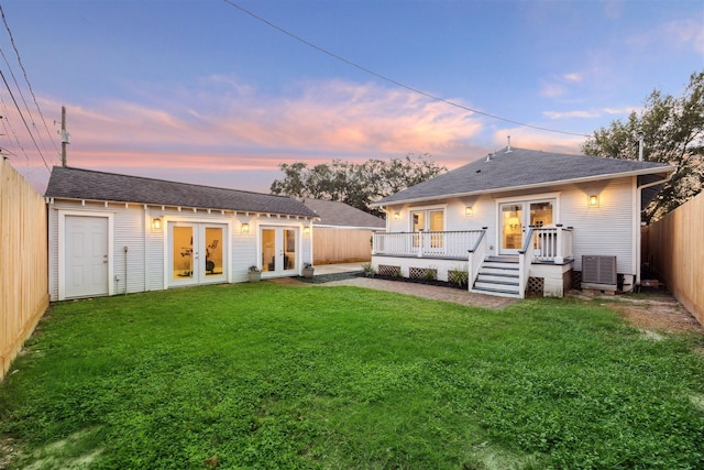 back house at dusk with a lawn, french doors, and a deck