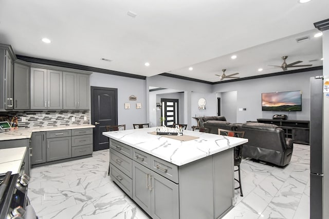 kitchen featuring a center island, tasteful backsplash, crown molding, gray cabinets, and a breakfast bar