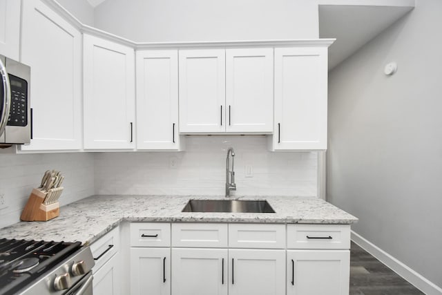 kitchen with white cabinets, backsplash, light stone countertops, and sink