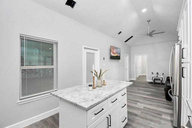 kitchen featuring white cabinets, a center island, vaulted ceiling, and light stone countertops