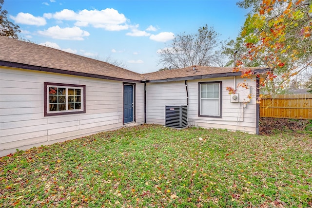 rear view of property with central air condition unit and a yard