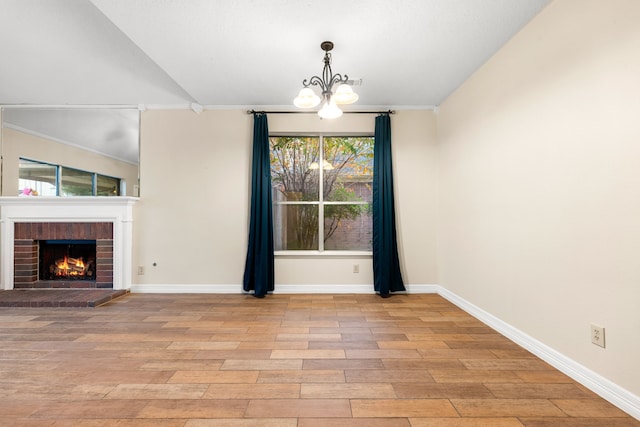 unfurnished dining area with lofted ceiling, a brick fireplace, ornamental molding, a notable chandelier, and light hardwood / wood-style floors