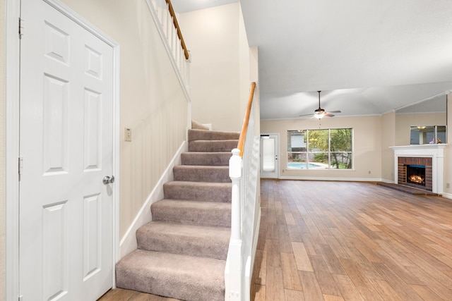 stairs featuring hardwood / wood-style floors, ceiling fan, ornamental molding, and a fireplace