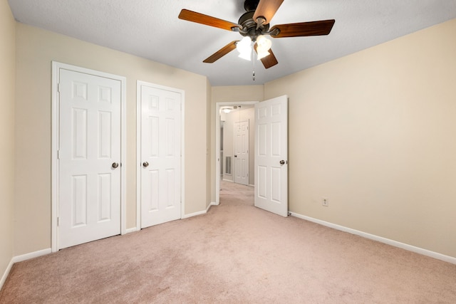 unfurnished bedroom featuring light carpet, two closets, and ceiling fan