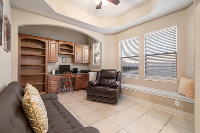 tiled home office with a raised ceiling, ceiling fan, and built in desk