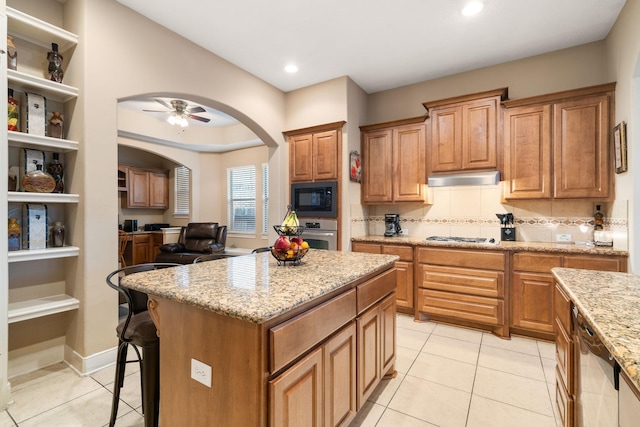 kitchen with black microwave, light stone countertops, ceiling fan, light tile patterned floors, and a kitchen island